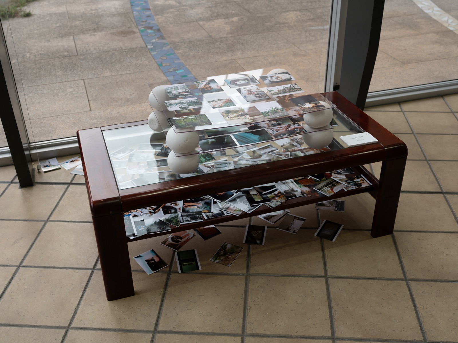 An installation: acrylic sheets held up by white spheres on a glass table, with photographs in several layers