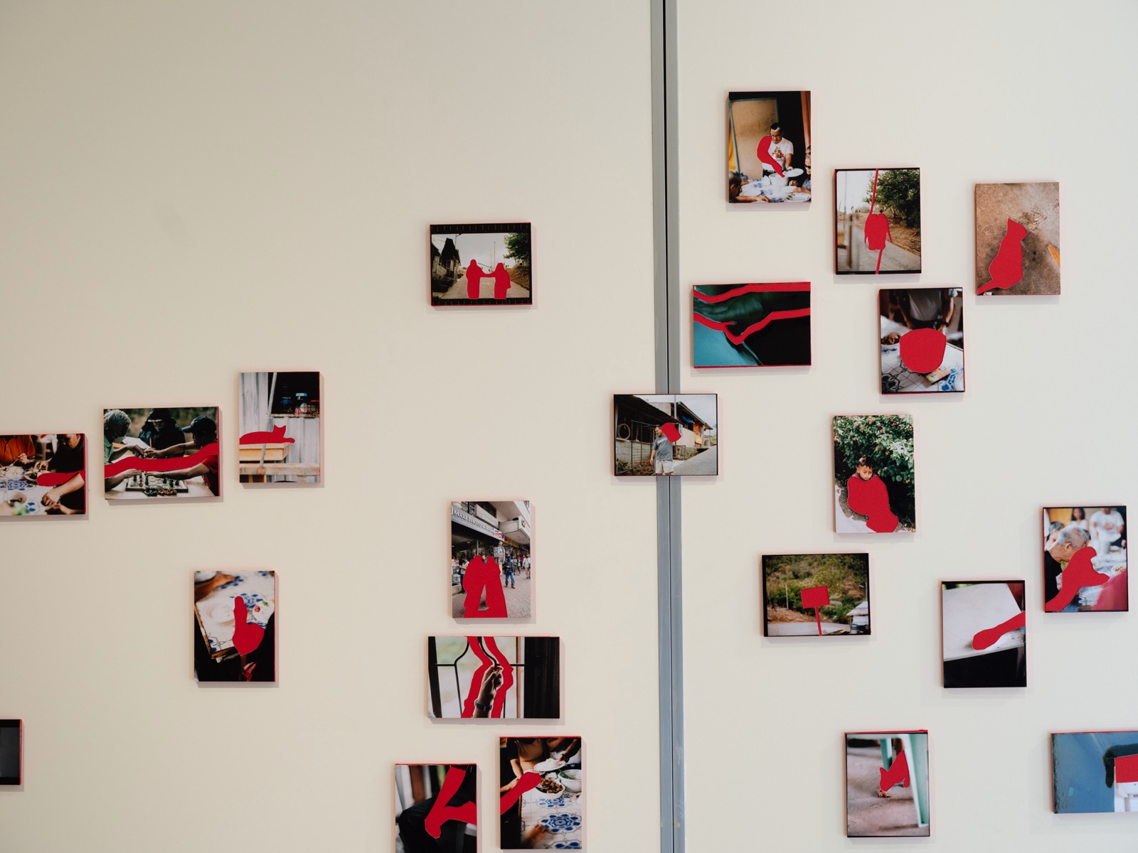 Photographs on a wall, each with the shape of a person, a hand or a cat cut out and marked in red